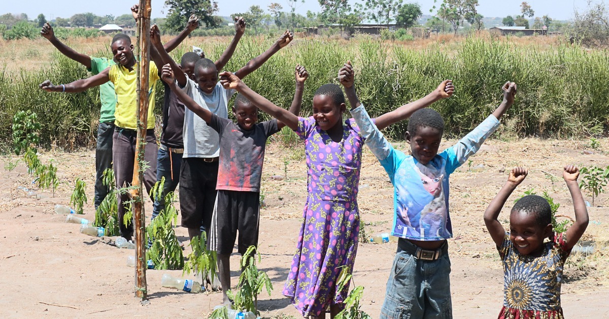 Children stand next to tree seedlings.
