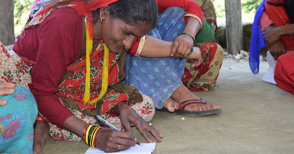 Panna Devi sits on the ground and writes with a pencil and a paper