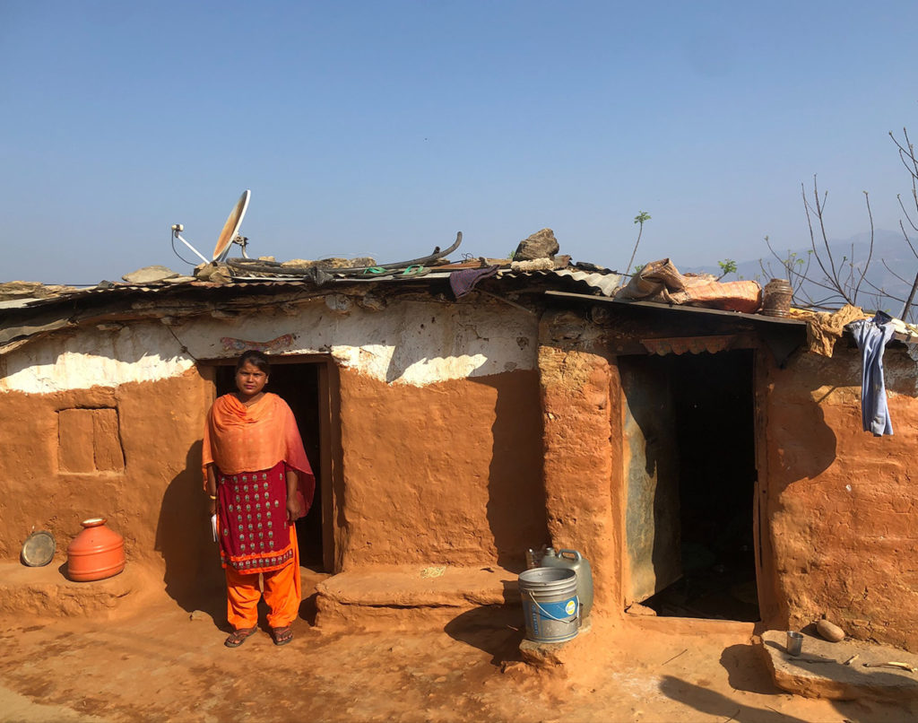 A Nepali woman standing in front of her simple home