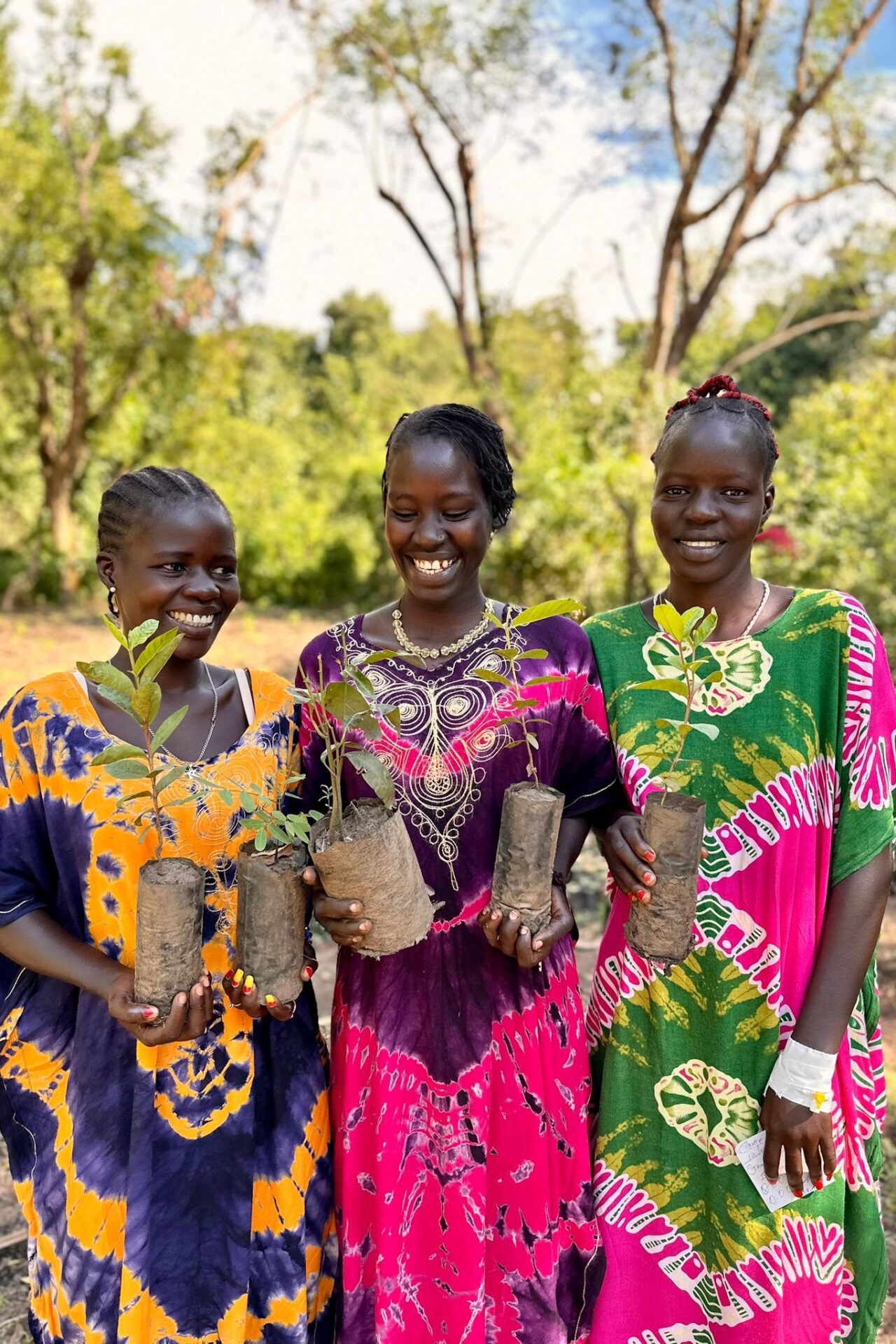 Three young women holding tree seedlings.